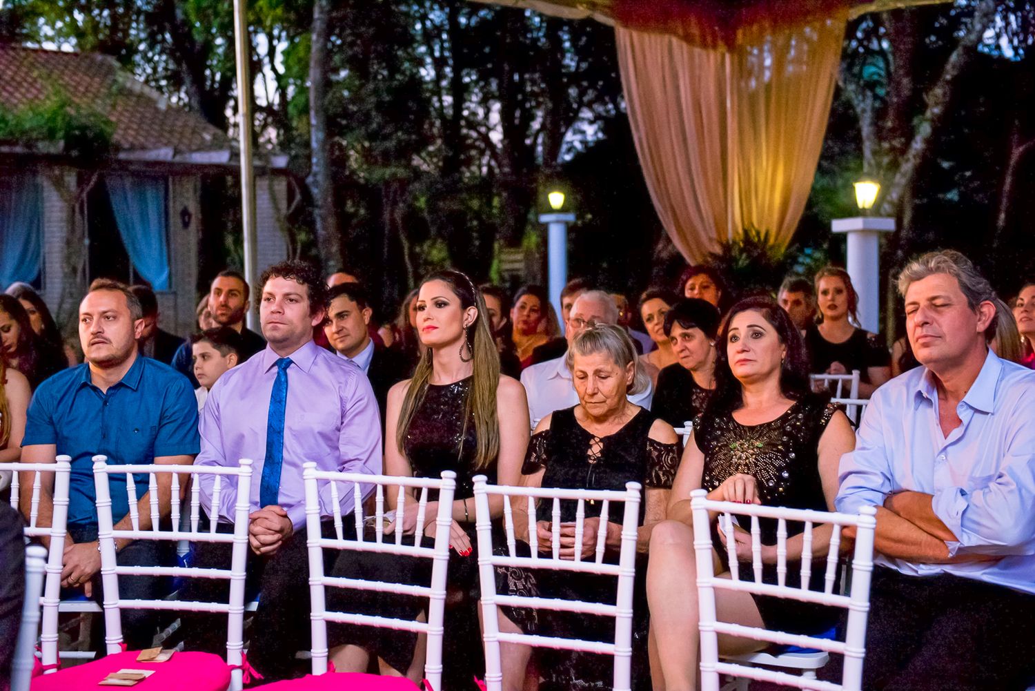 Wedding guests seated in white chairs watching ceremony under elegant outdoor tent setup.