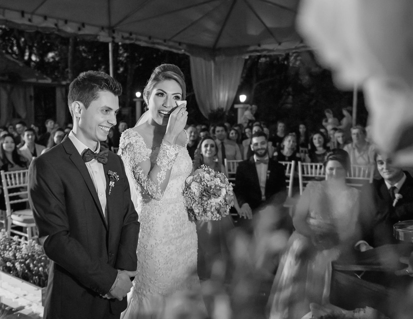 Wedding couple shares an emotional moment during ceremony while guests look on from white chairs.