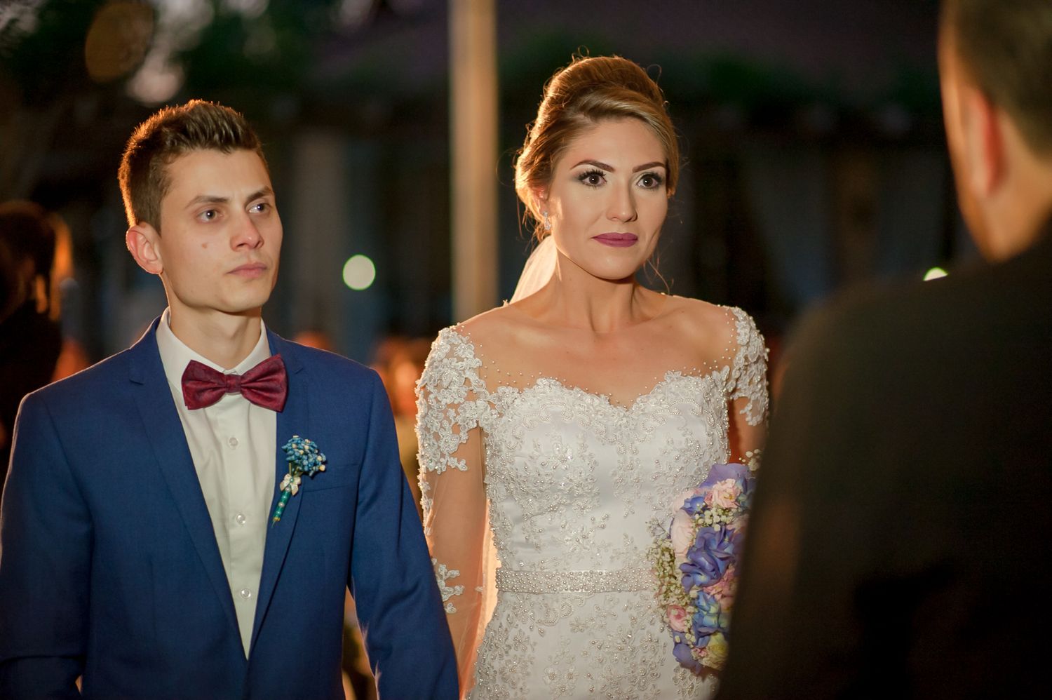 Couple in formal wedding attire listens intently during evening ceremony.