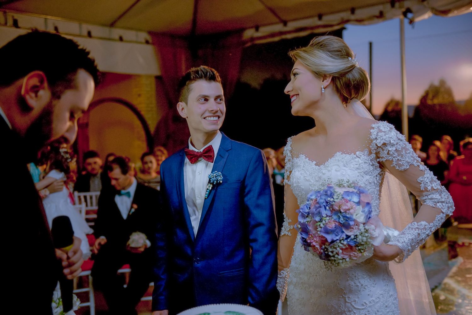 Wedding party in blue and white attire exchanges smiles during outdoor ceremony.
