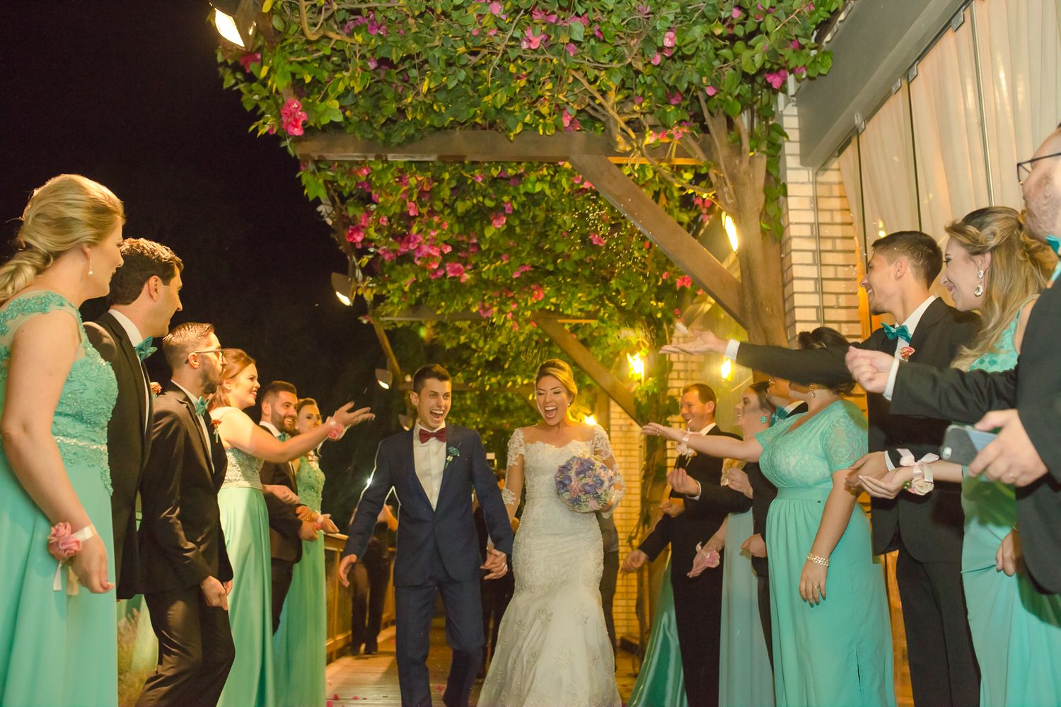 Wedding party in mint green dresses forms walkway under flowering tree at night.