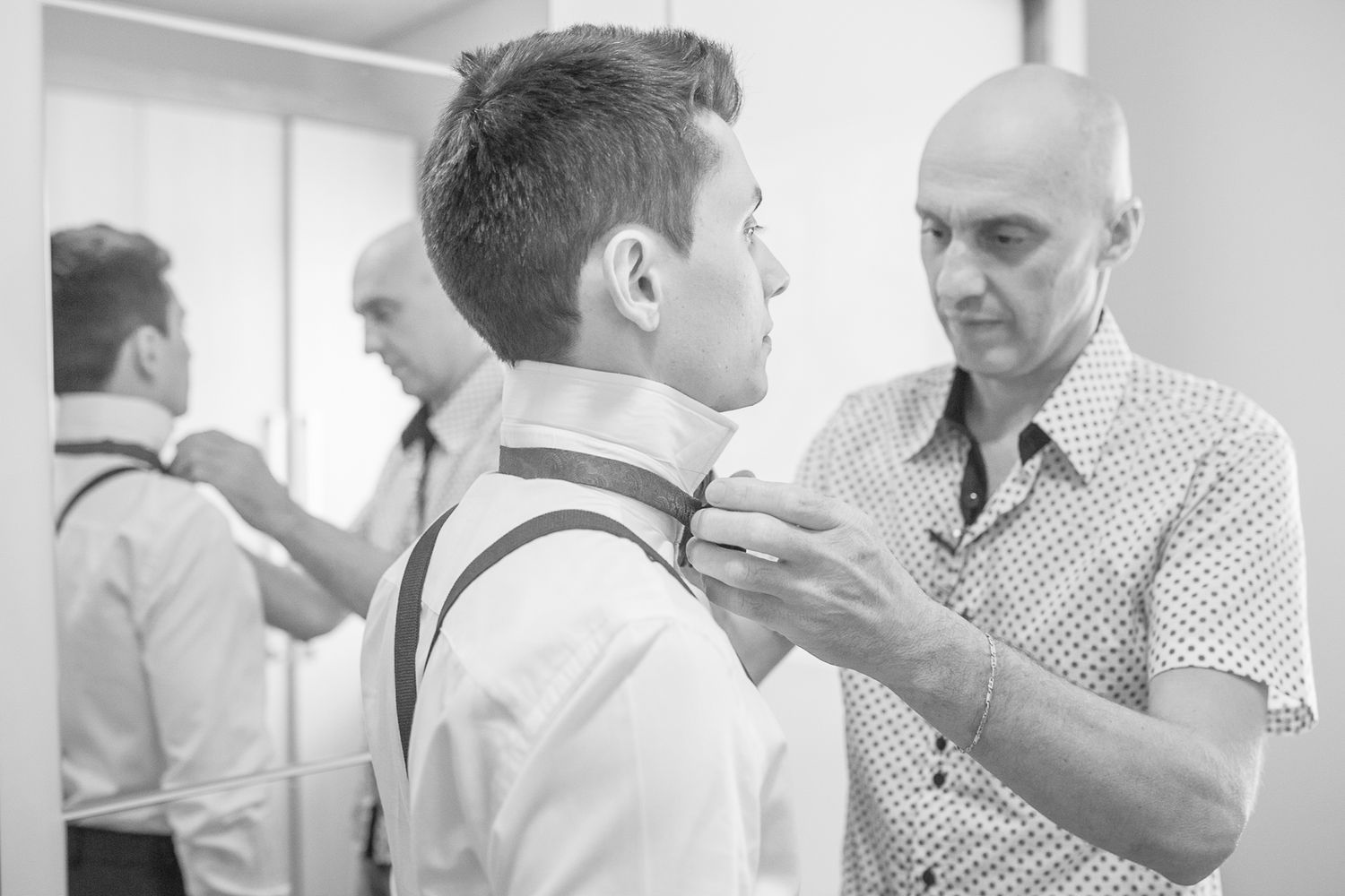 A stylist adjusts the bow tie and suit on a groom before the wedding ceremony.