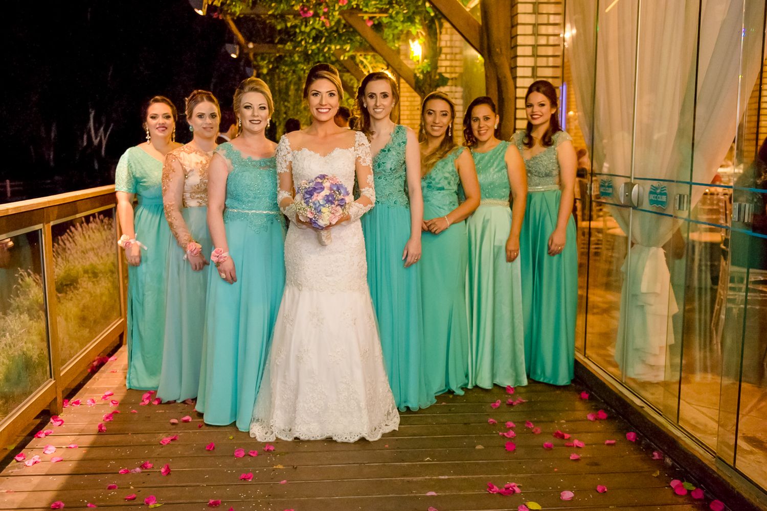 Bridesmaids in matching turquoise dresses pose with bride in white gown on outdoor deck.