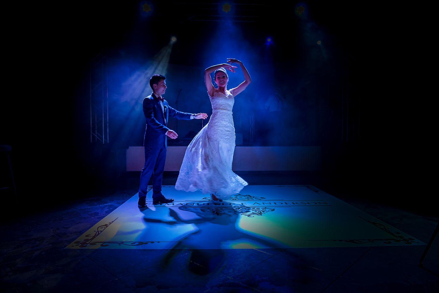 Couple performs first dance under dramatic blue stage lighting at wedding reception.