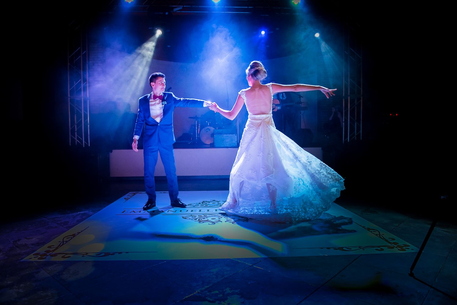 Newlyweds dance together on illuminated stage with dramatic blue lighting effects.