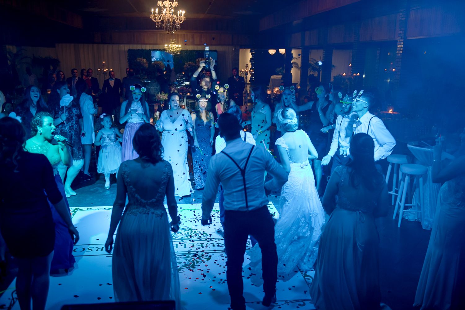 Wedding reception dance floor filled with guests under blue ambient lighting.