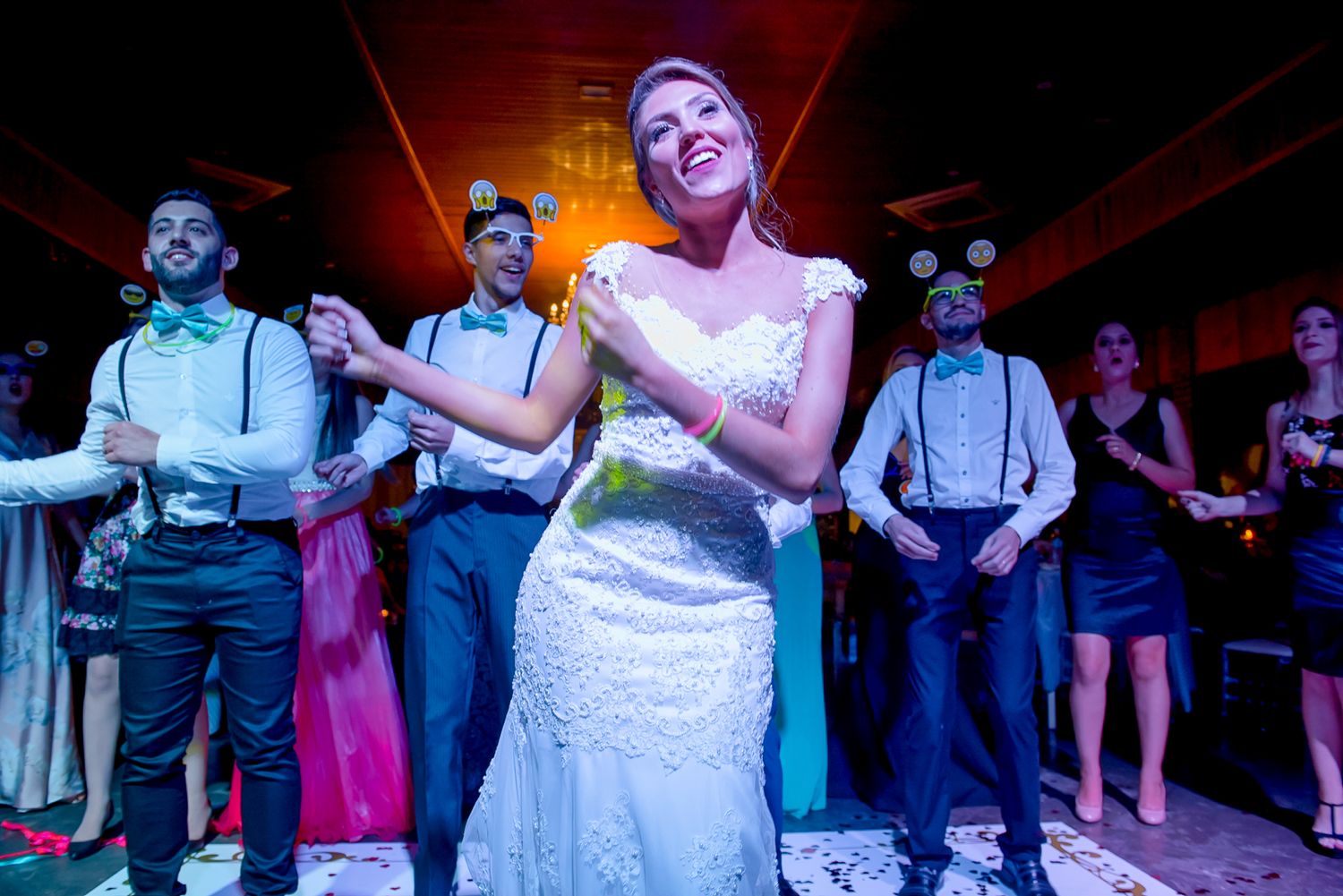 Wedding party performs choreographed dance routine under red stage lighting.