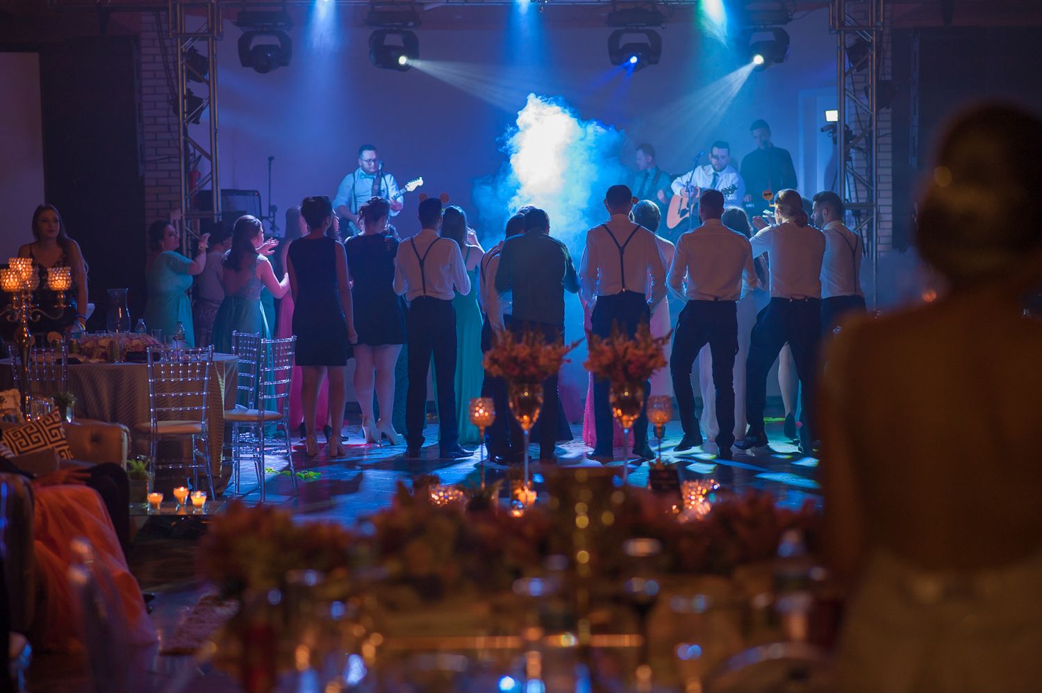Silhouetted wedding guests dance on smoky, blue-lit dance floor.