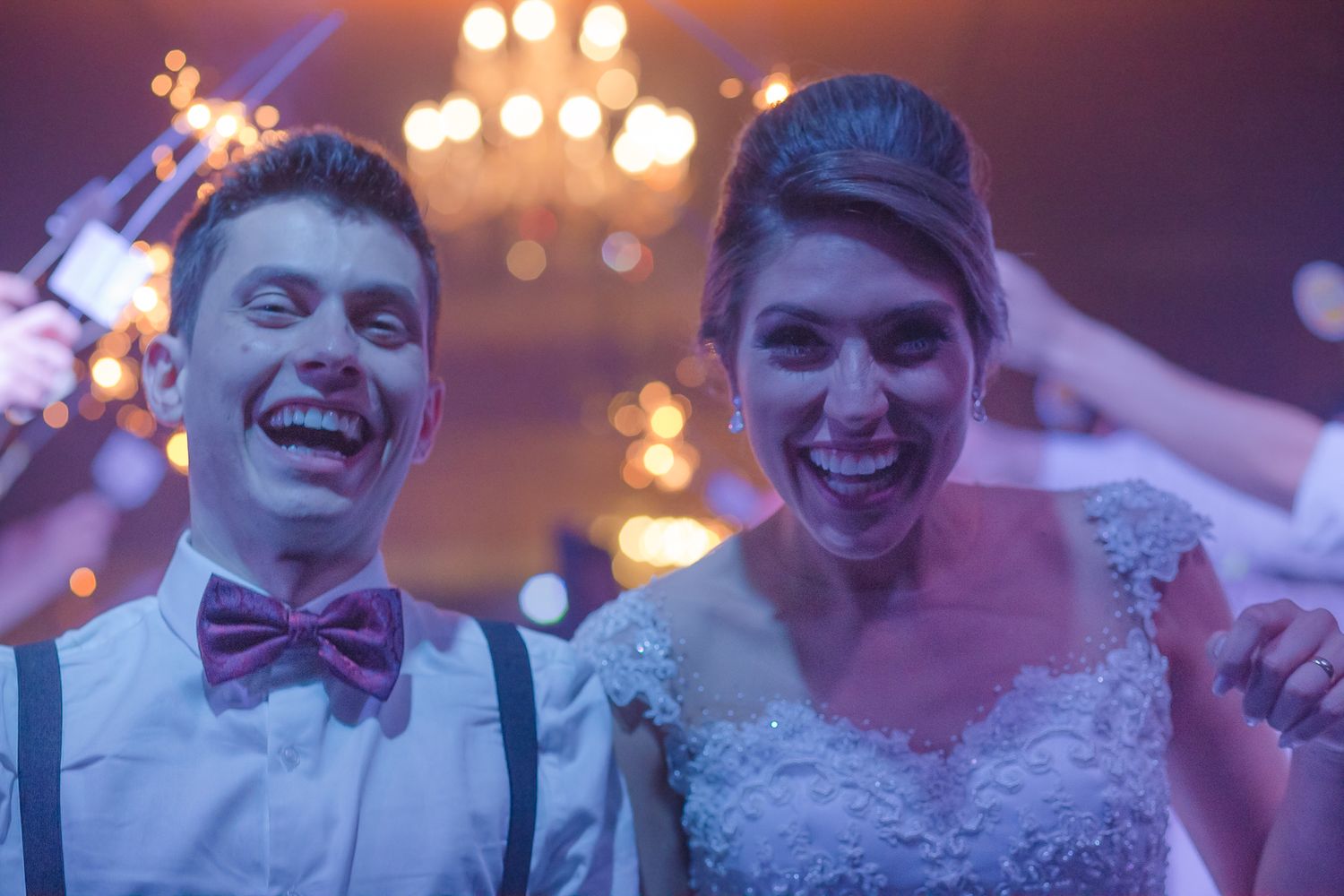 Newlyweds celebrating under warm chandelier lights at wedding reception.
