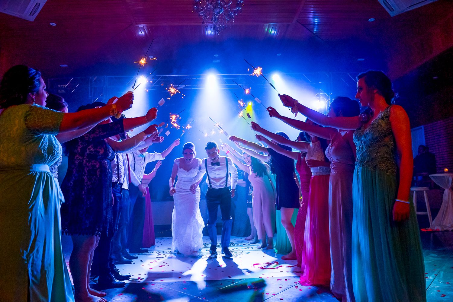 Wedding guests create sparkler tunnel with colorful blue lighting for dancing couple.