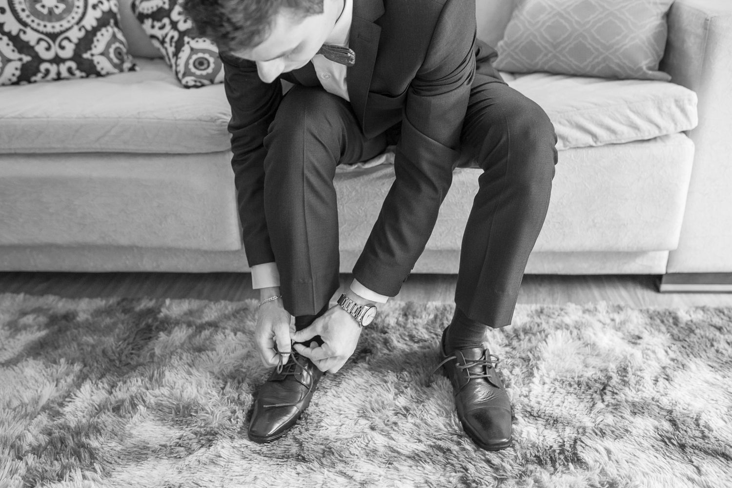 Black and white photo of someone tying dress shoes while sitting on an elegant sofa.