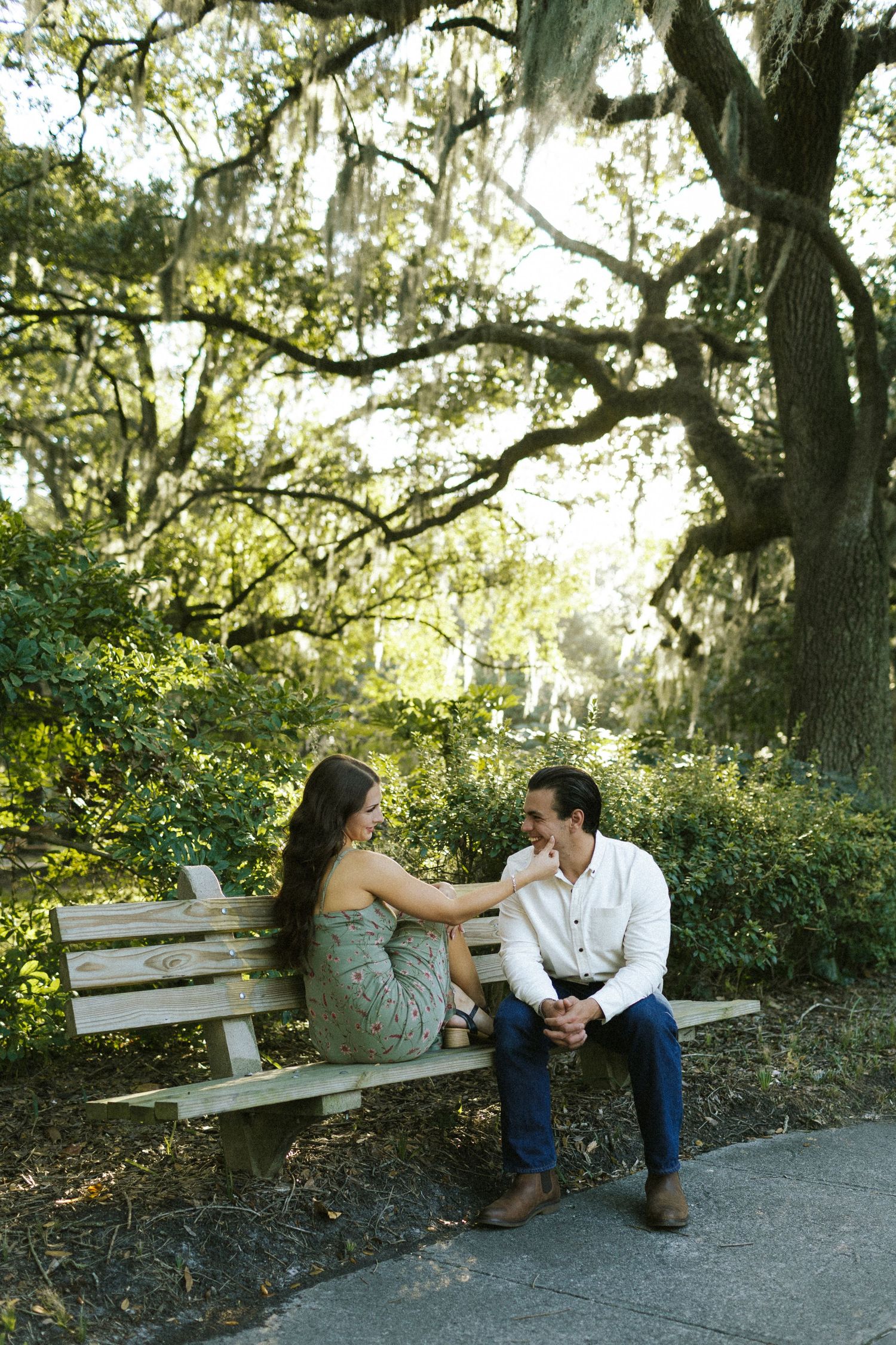 A couple sitting on a park bench, the woman caresses the face of the man as they face toward each other