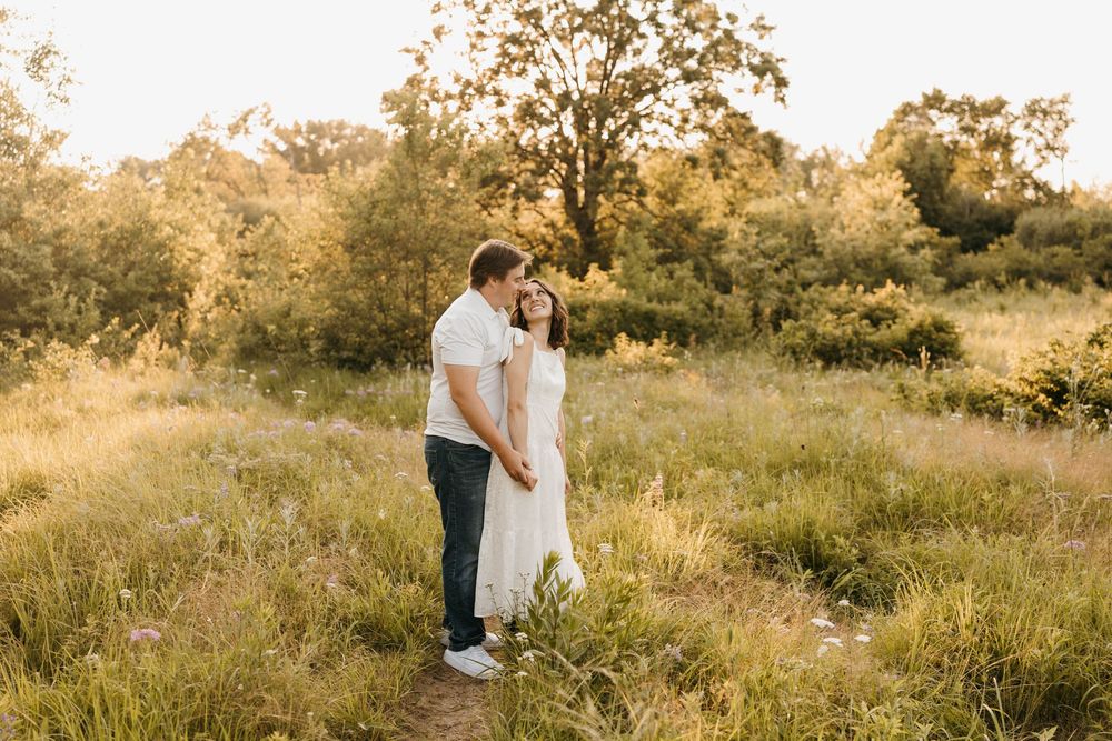 Couple holding hands in golden hour sunlight in a lush green meadow during engagement photo session.