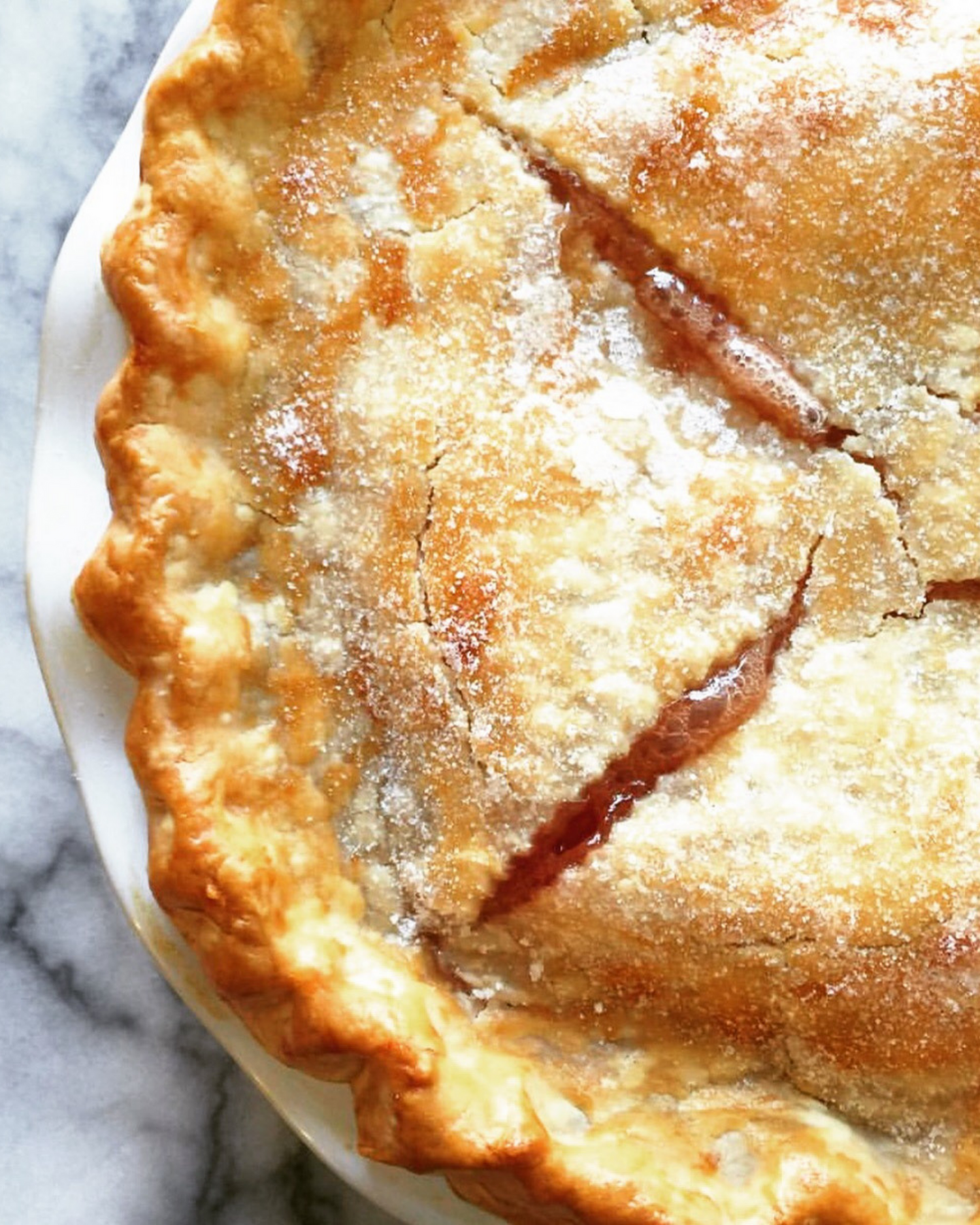 Golden brown peach pie with lattice crust dusted with sugar on a marble surface.