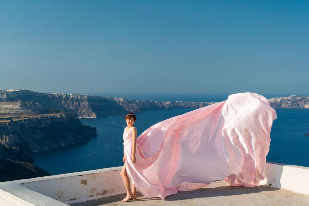 Pink flowing fabric against white architecture overlooking Santorini caldera.
