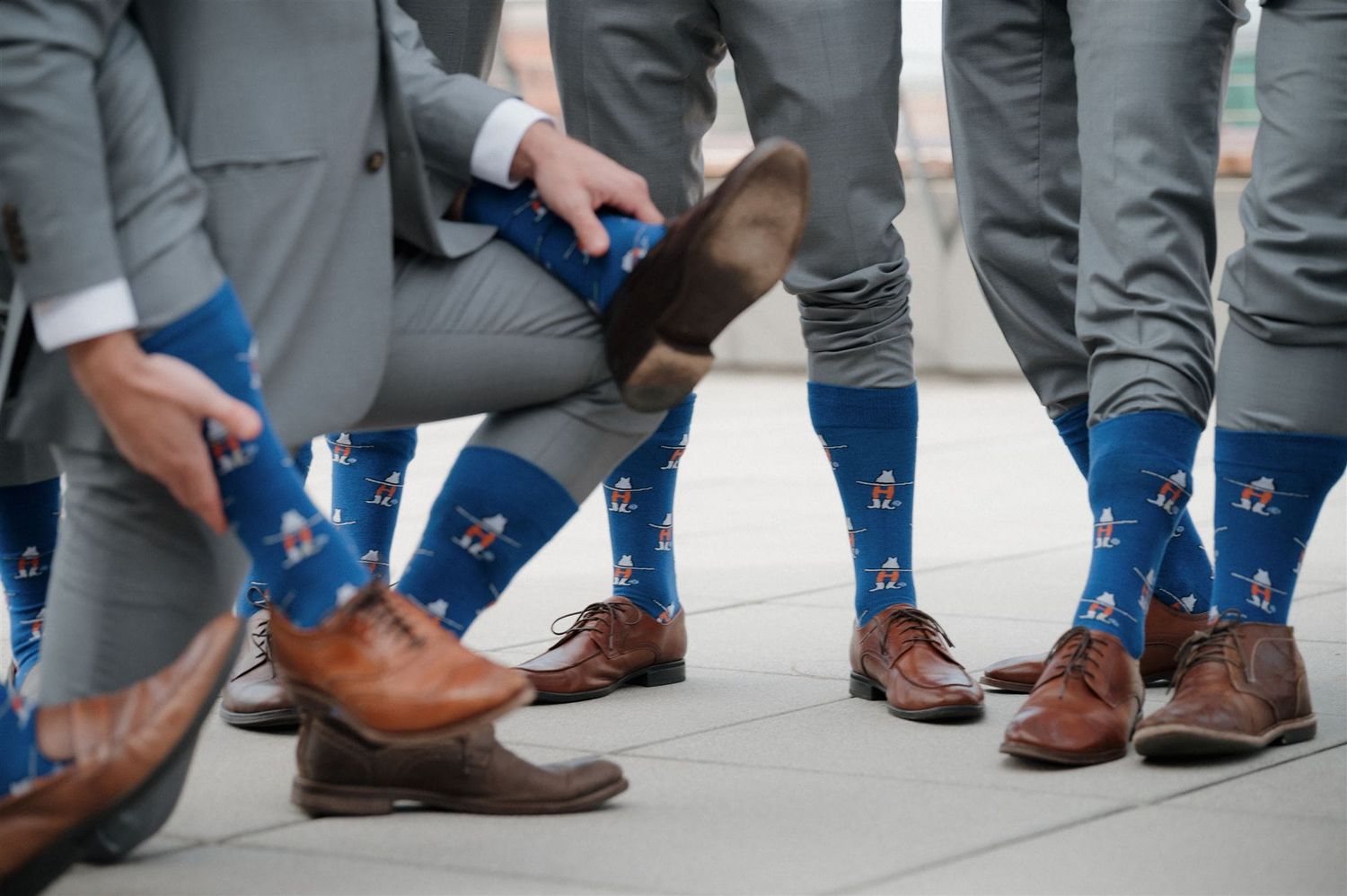 Groomsmen wearing matching blue star socks and brown leather dress shoes stand together in a circle showing off their fun attire.