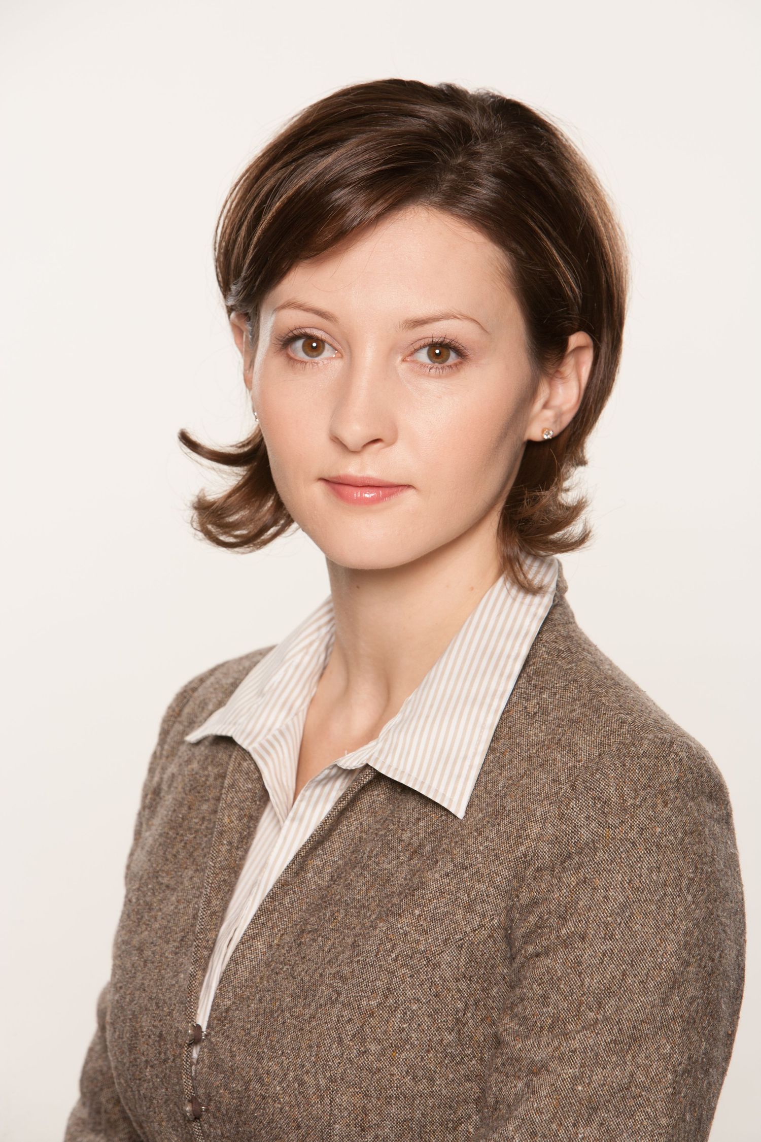 Professional portrait of person wearing brown sweater and striped collared shirt against white background.