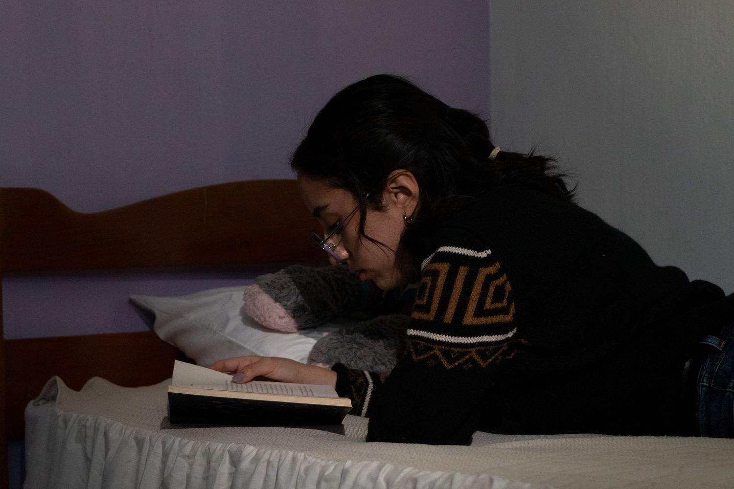 Reader lying down with book in shadowy room.