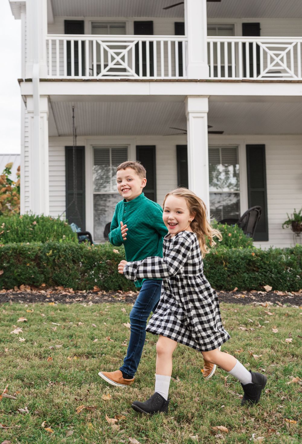 Fall portrait of children running and laughing together in front of a historic house.