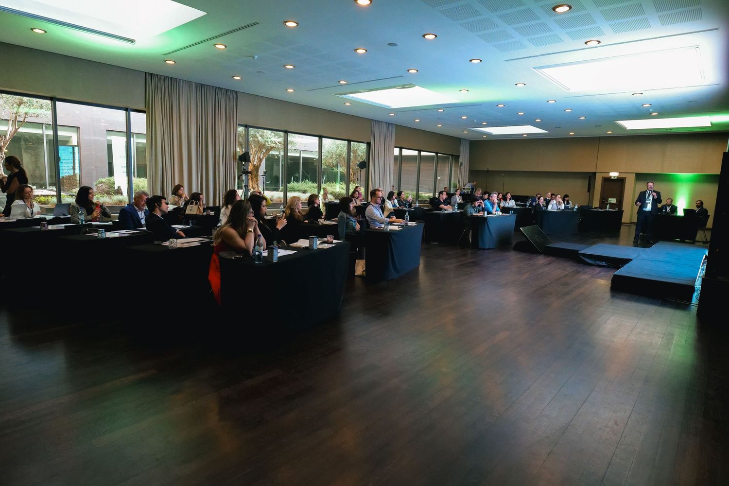 Wide-angle view of attendees at a dimly lit professional conference in a modern event hall.
