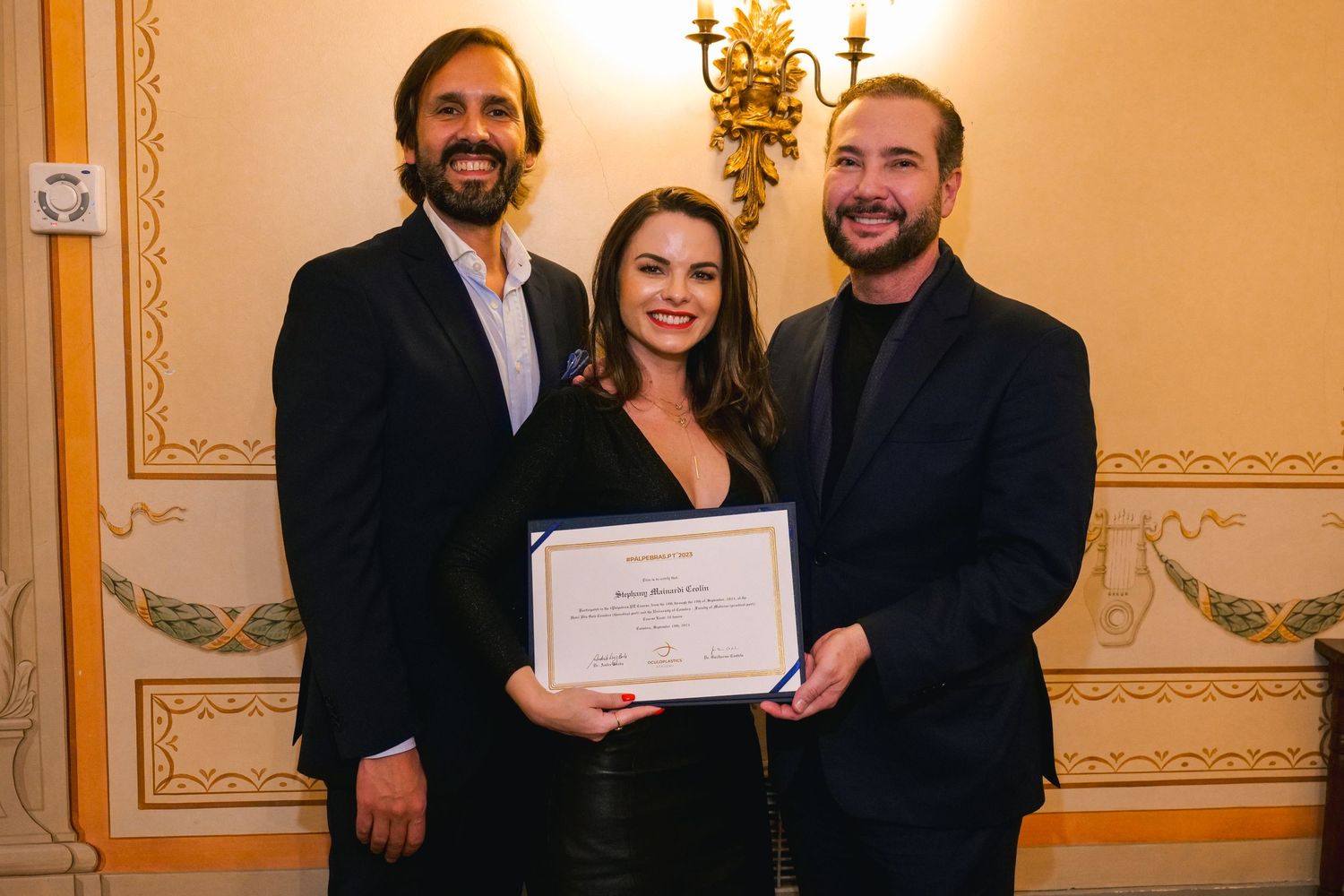 Two men and a woman proudly holding a certificate at a formal awards ceremony indoors.