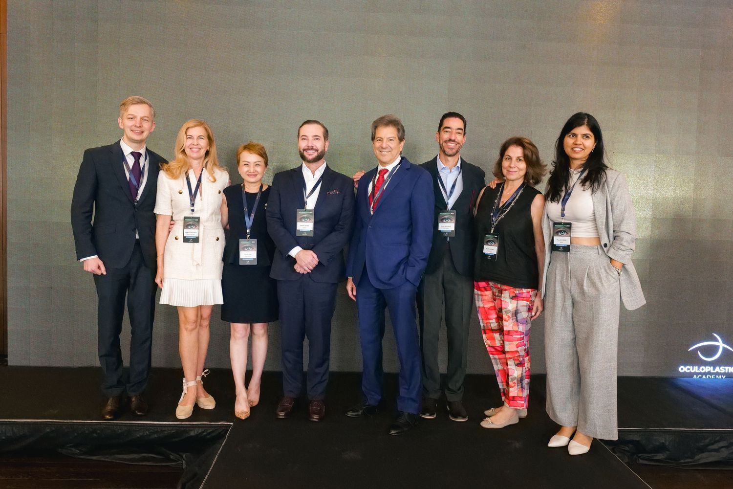 Group of eight medical professionals in formal attire posing together at a conference event.