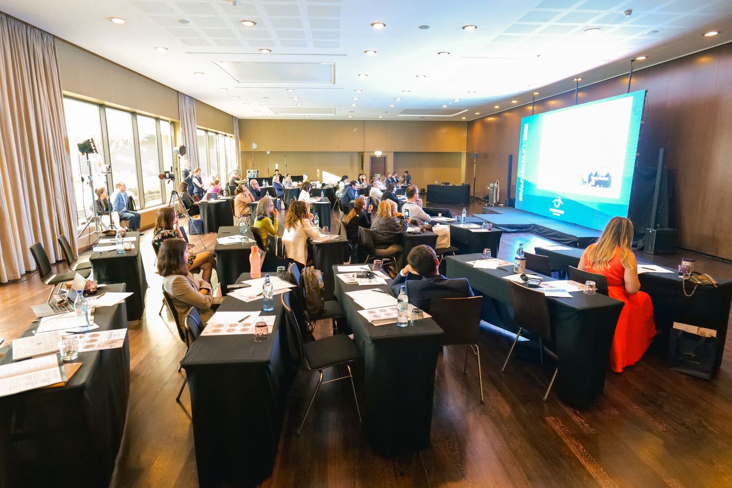 Attendees seated at tables during a medical conference session with a presentation screen displayed.