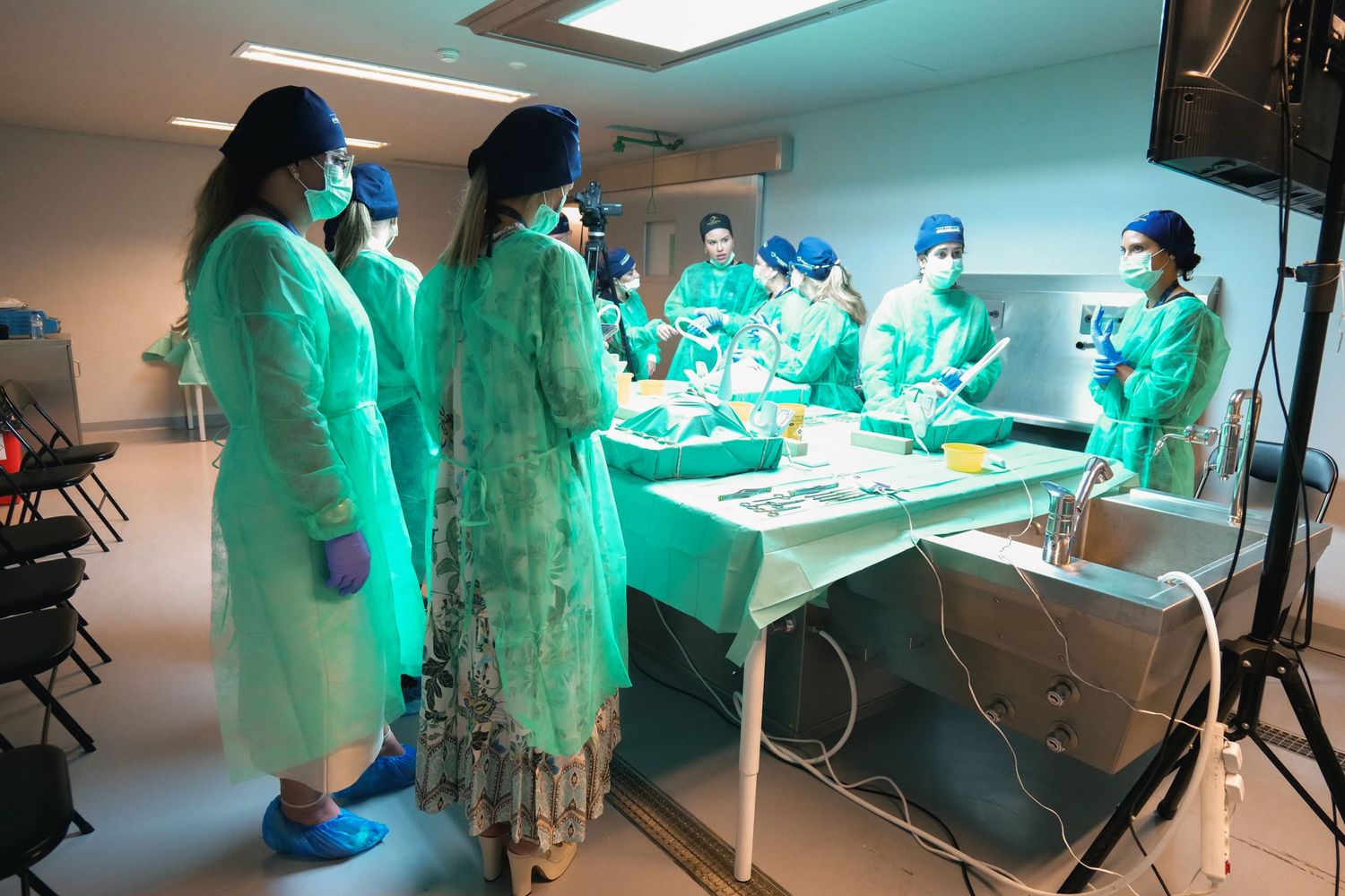 Medical students in green surgical gowns observing a live surgical procedure demonstration in a lab.