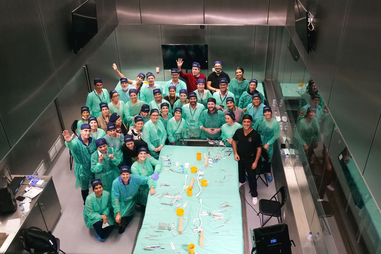 Large group of medical students in green scrubs pose for a photo in a surgical training lab.