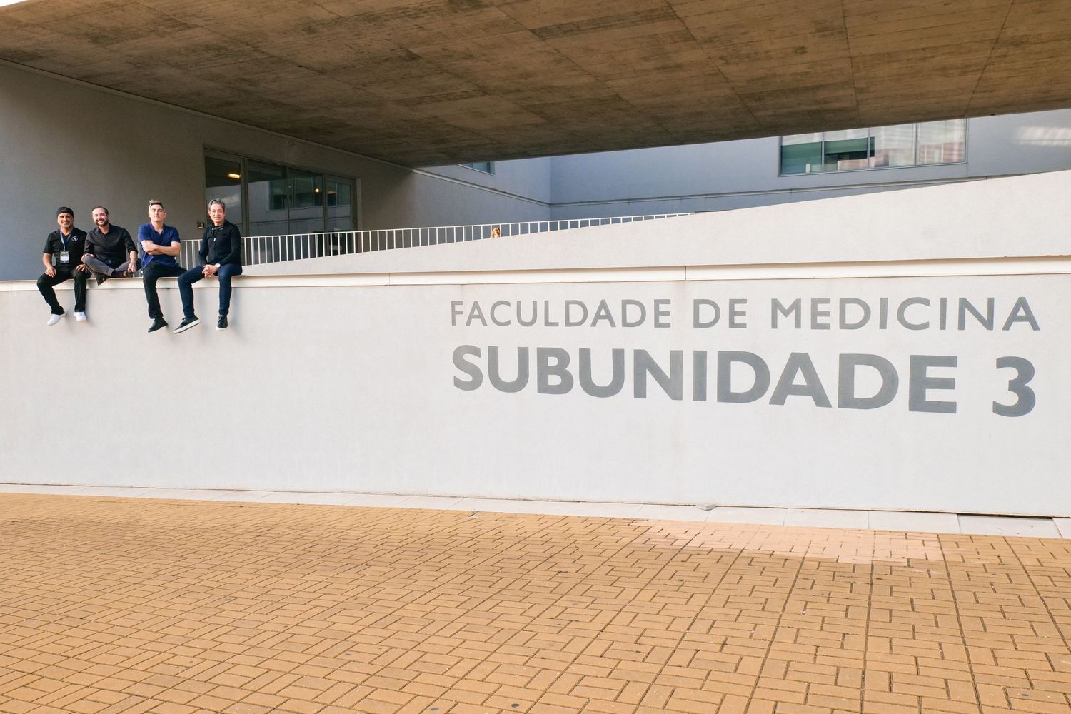 Four people sit on the wall of Faculdade de Medicina Subunidade 3 building exterior.