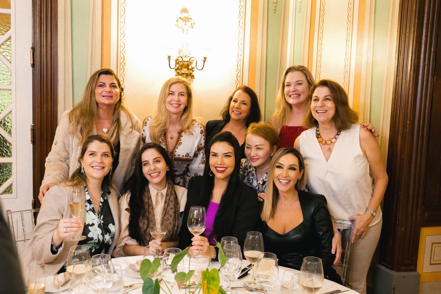 Group of ten women posing together and smiling at an elegant formal dinner celebration.