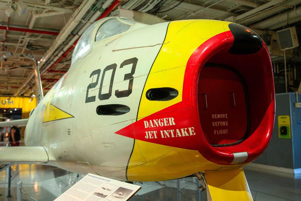 Close-up view of a red air intake on a vintage military aircraft with danger warning.
