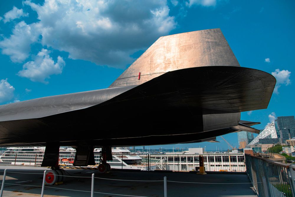 Dramatic view of an SR-71 Blackbird aircraft nose cone against blue sky.