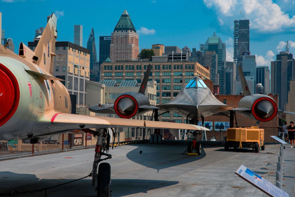 Vintage aircraft displayed at outdoor museum with urban skyline in background.