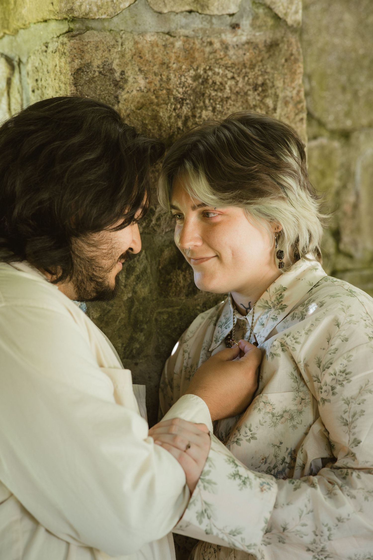 a husband holding the necklace of his bride that has their engagement rings on, as they stare loving back at each other