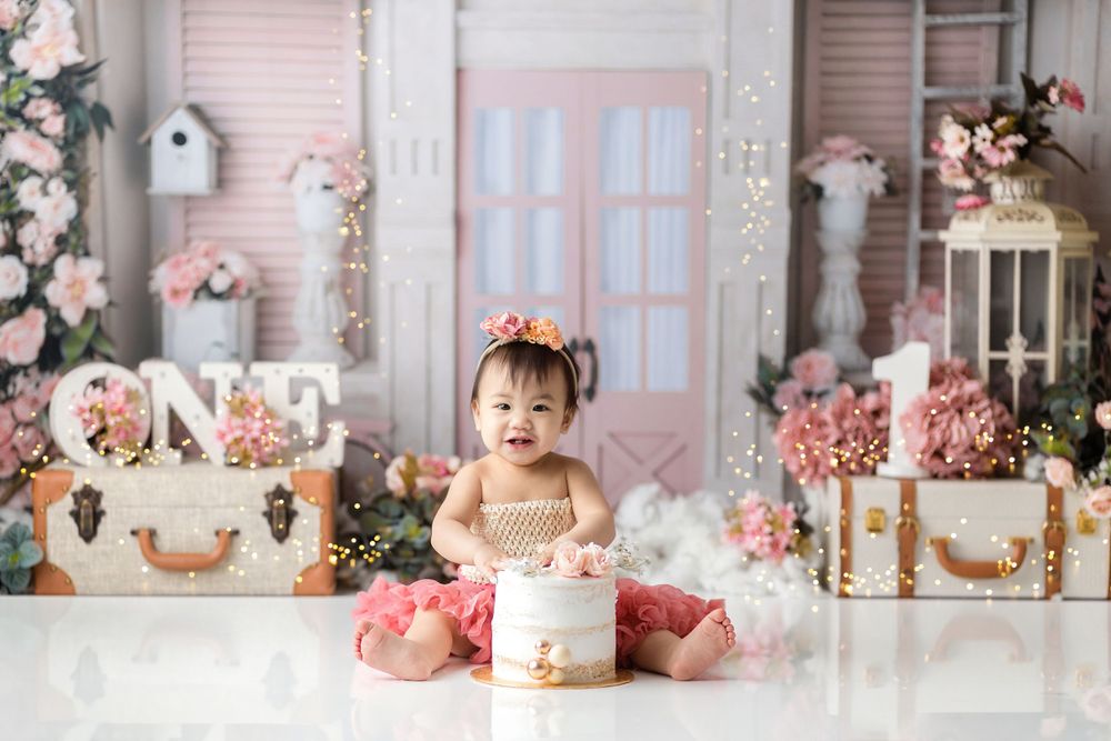 Baby's first birthday setup with pink floral decorations, vintage suitcases, and dreamy backdrop.