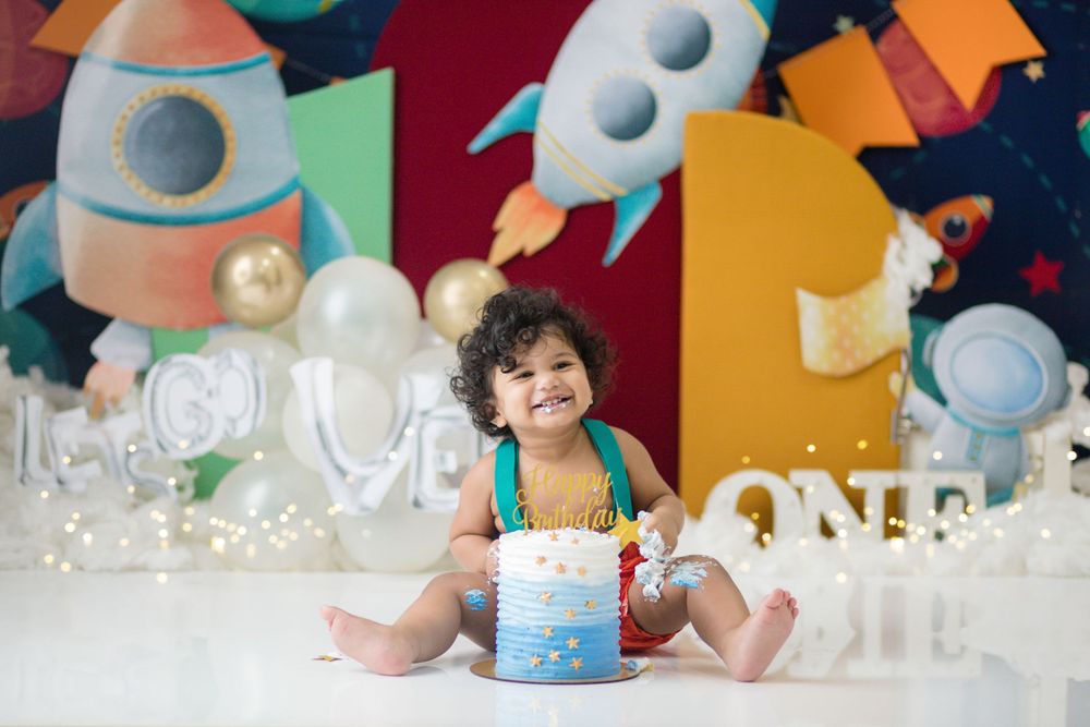 Space themed birthday setup with rocket ships, balloons, and colorful geometric backdrop.