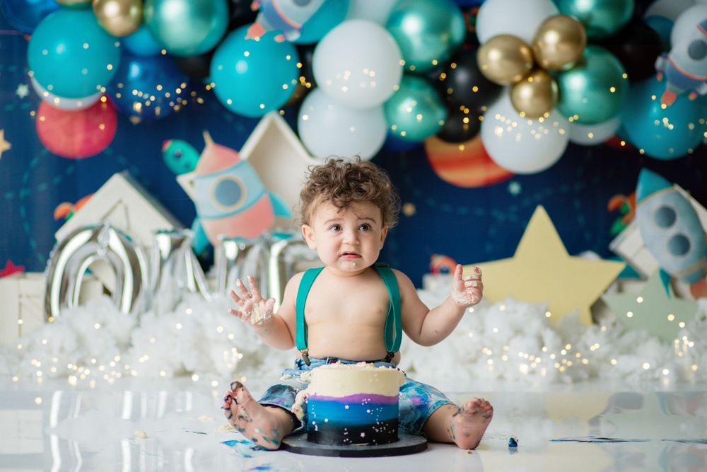Space themed cake smash photoshoot with teal and gold balloon arch and stars.