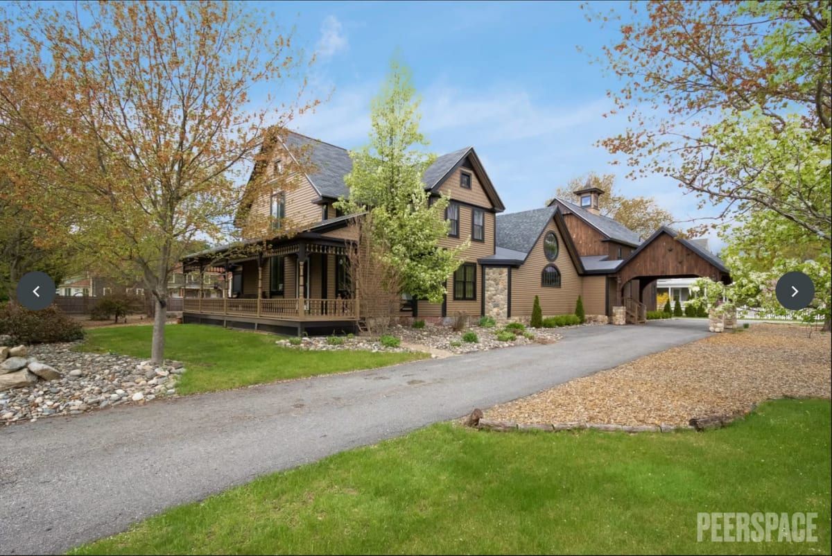 Luxurious farmhouse-style home with wrap-around porch and attached garage nestled among trees on a landscaped property.