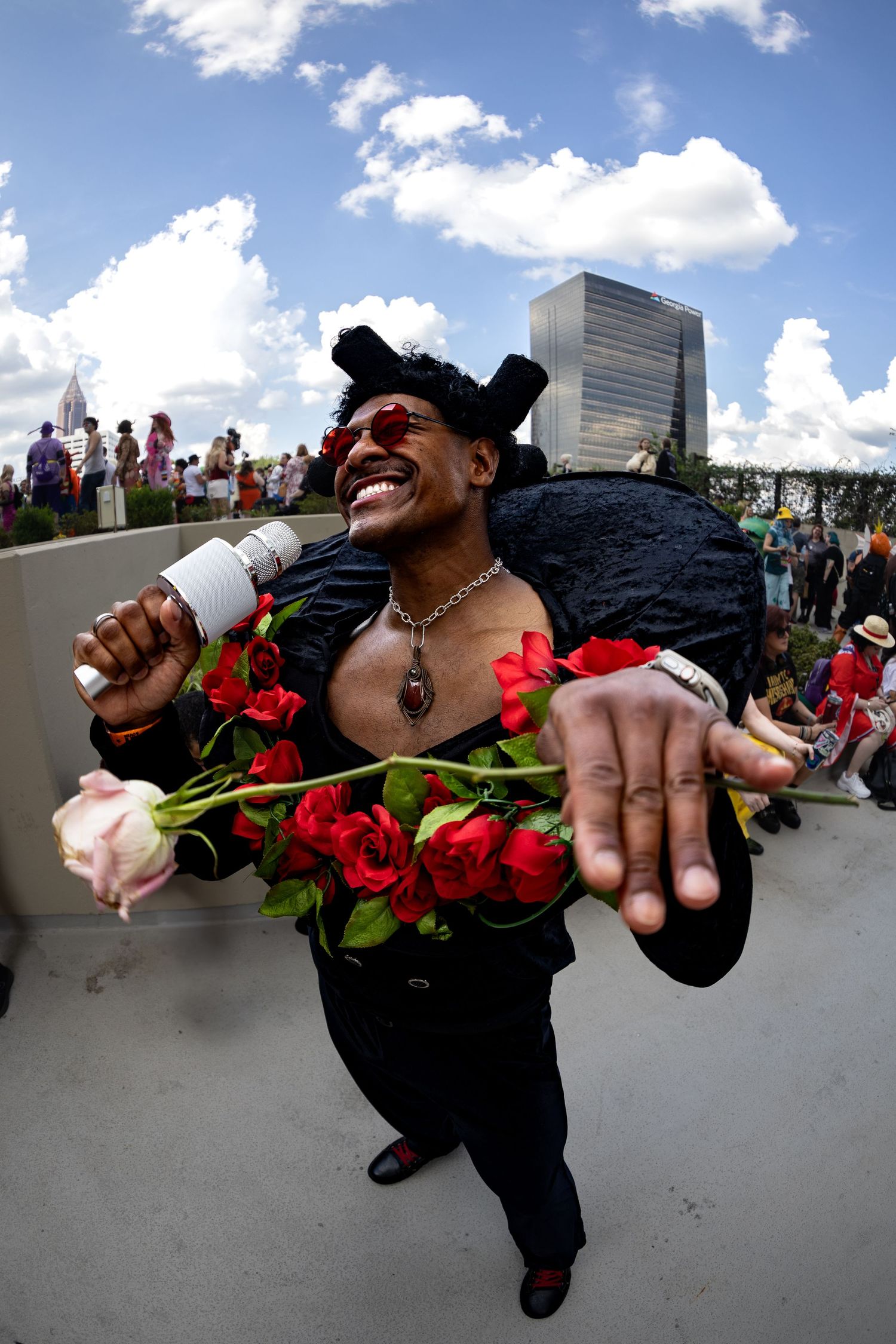 Performer holding microphone and roses with joyful expression against cloudy sky. | Shot By Lo™