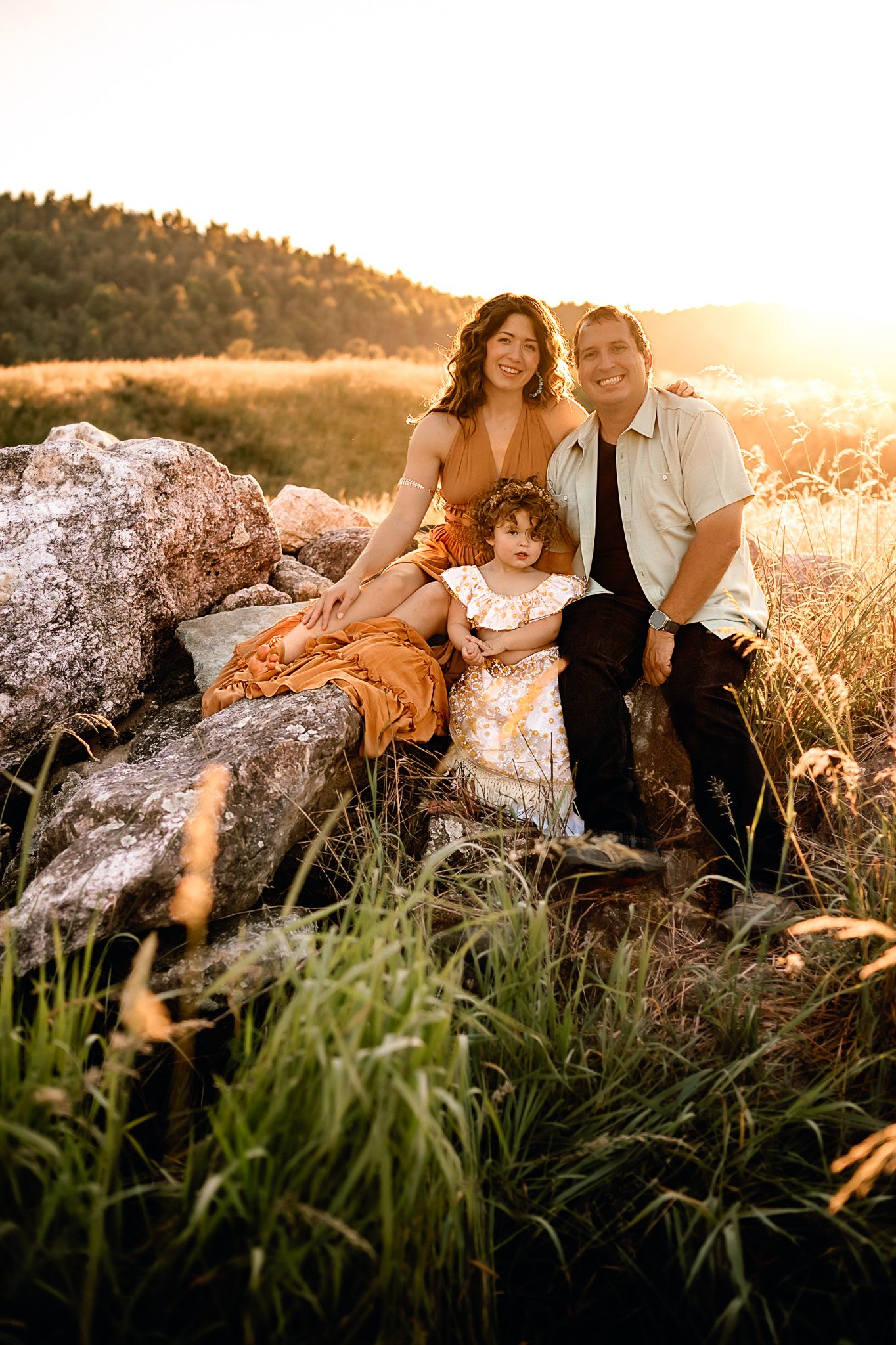 Family sitting together on rocks during golden hour sunset photoshoot.