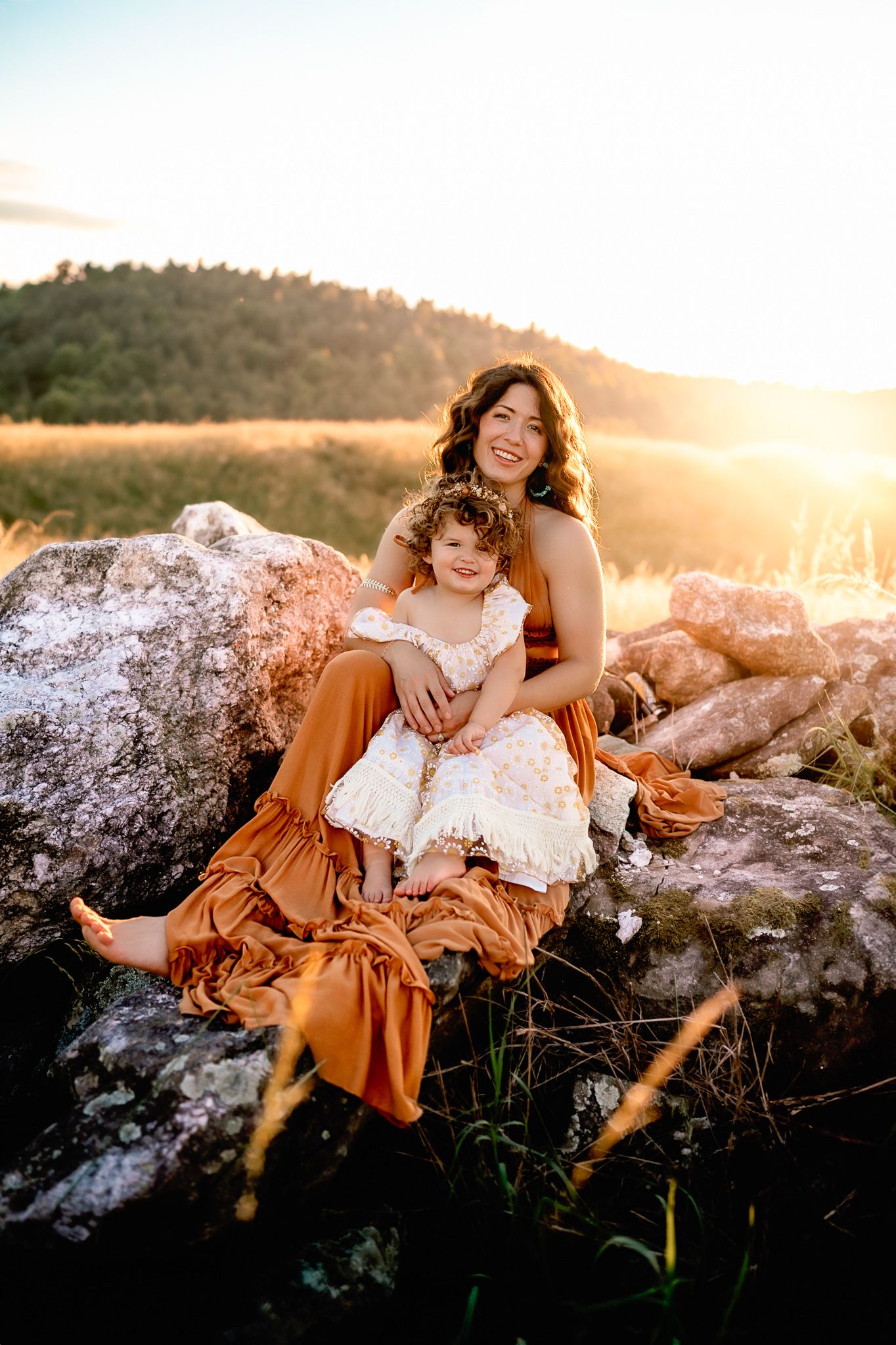 Mother and child sitting on rocks during sunset photo session.