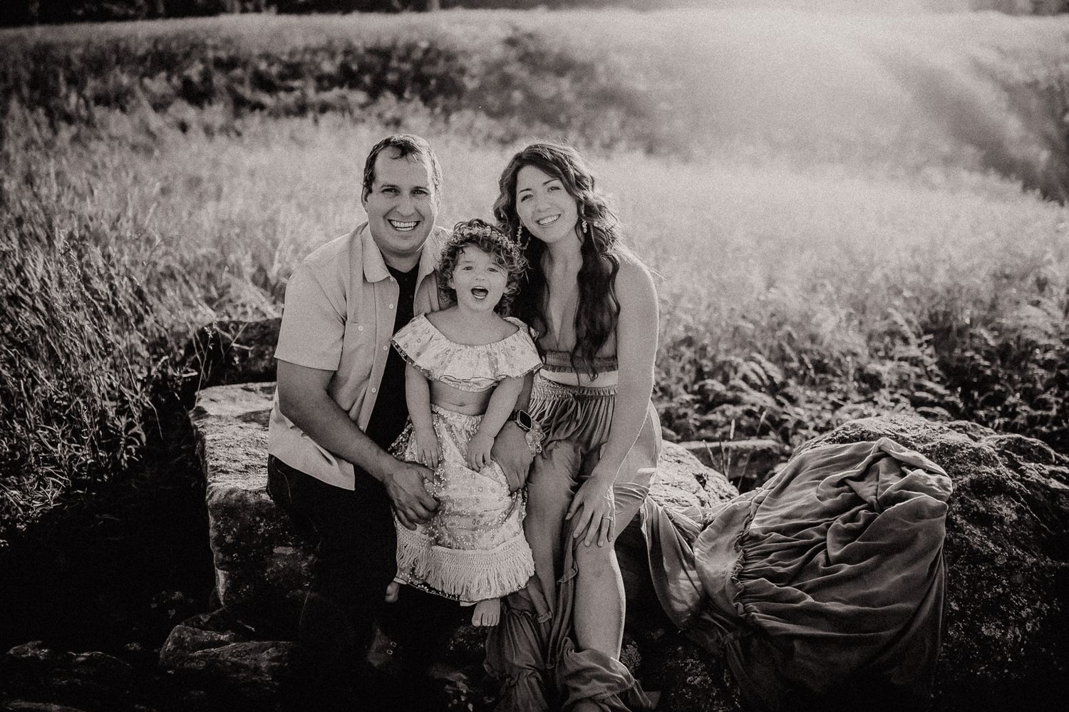 Family photo shoot in a field with wildflowers and soft light at sunset.