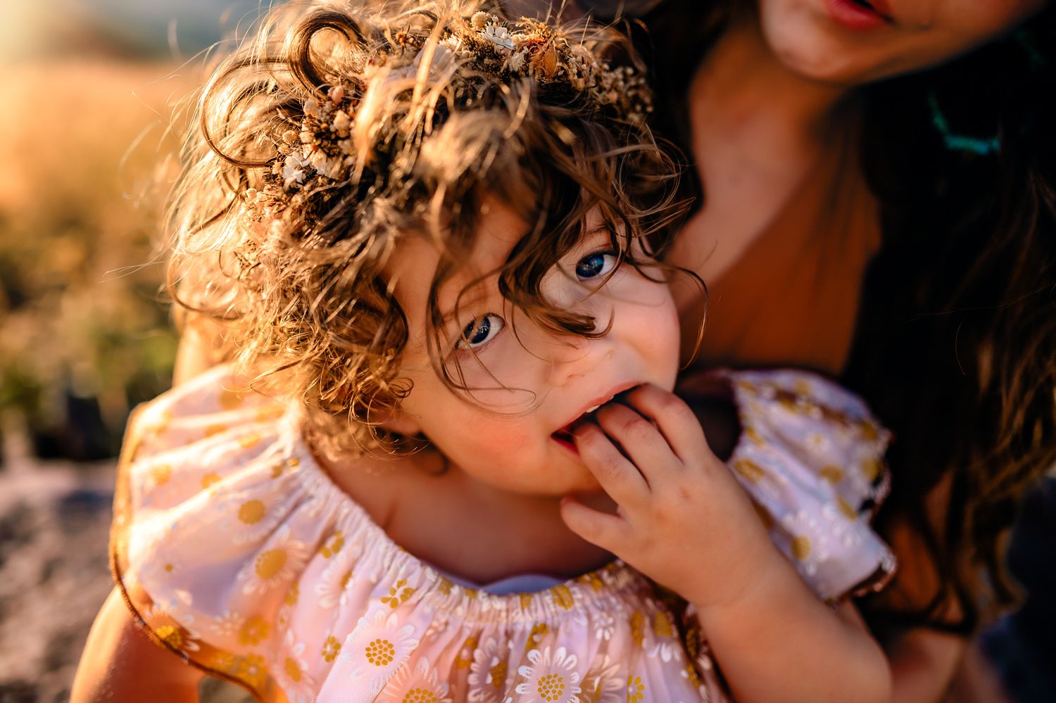Close-up of curly-haired child in floral dress with playful expression.