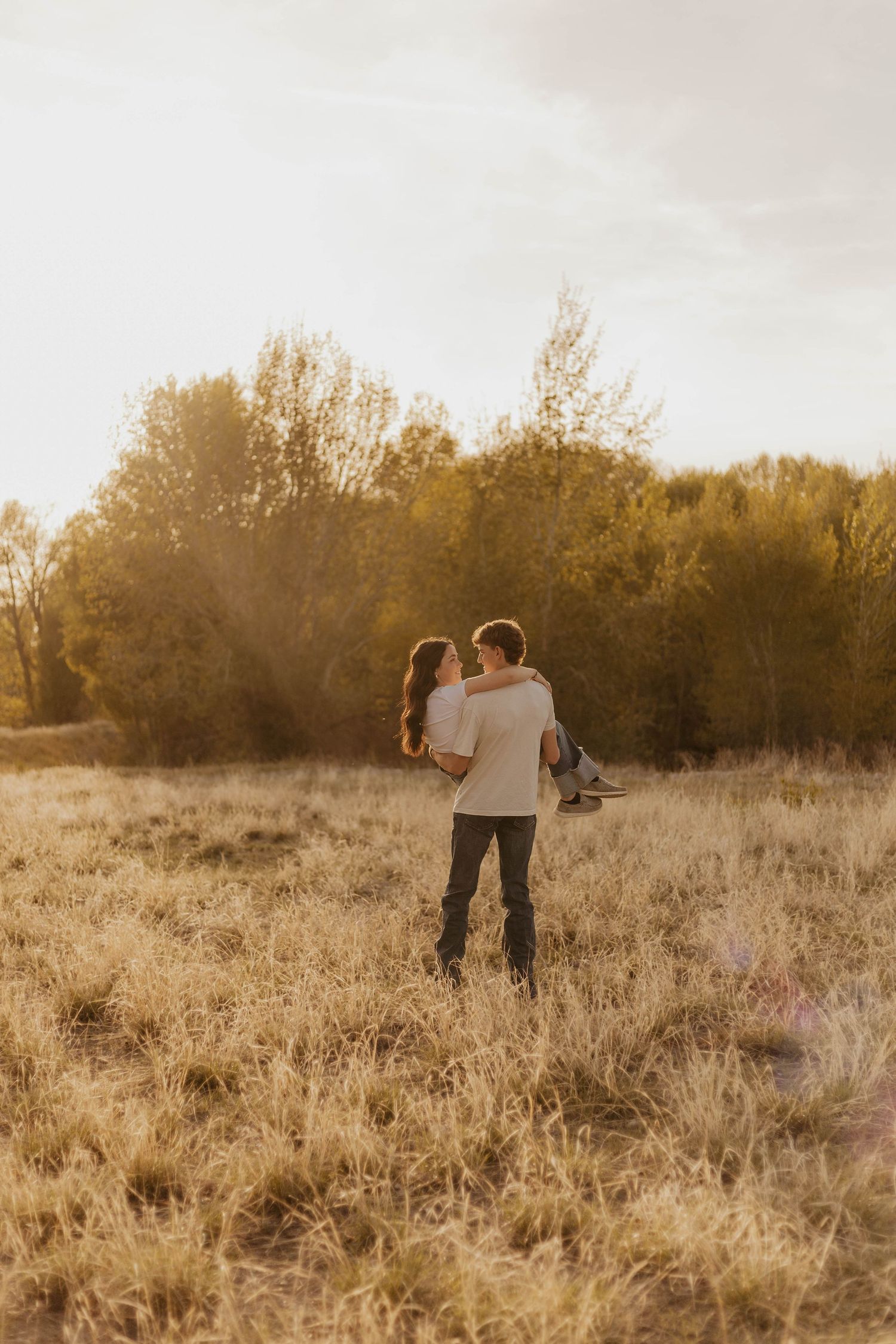 Western couple walking together through a serene autumn field with trees in the background.