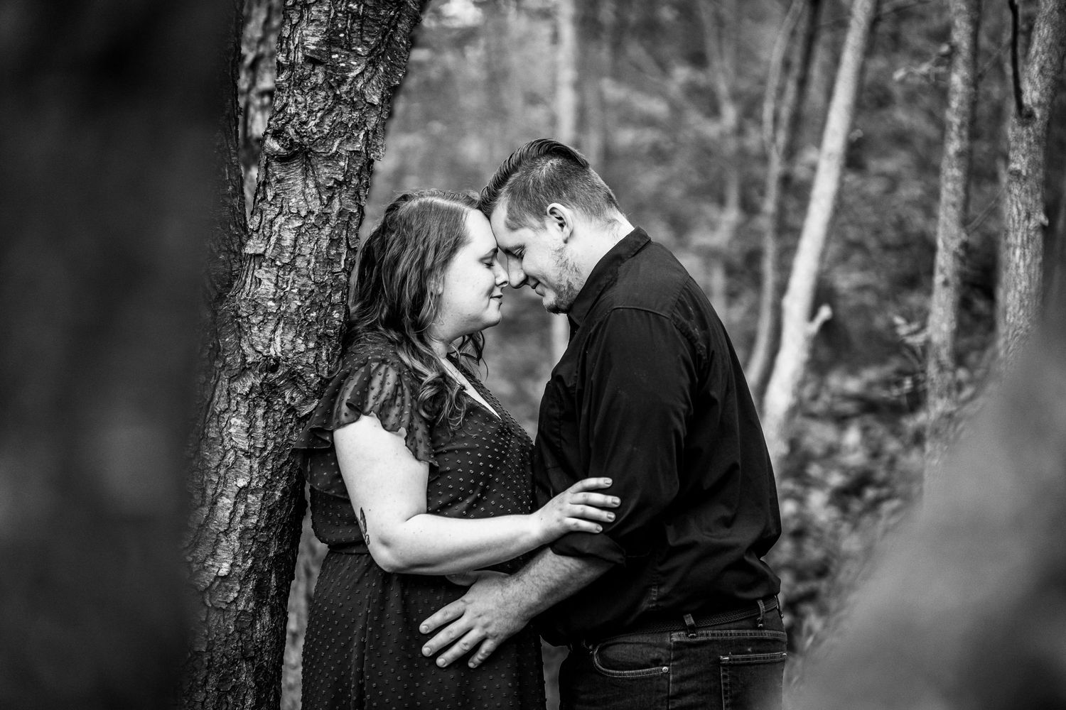 Black and white photo of a romantic couple sharing an intimate moment together among trees in a forest setting. unique couples photos