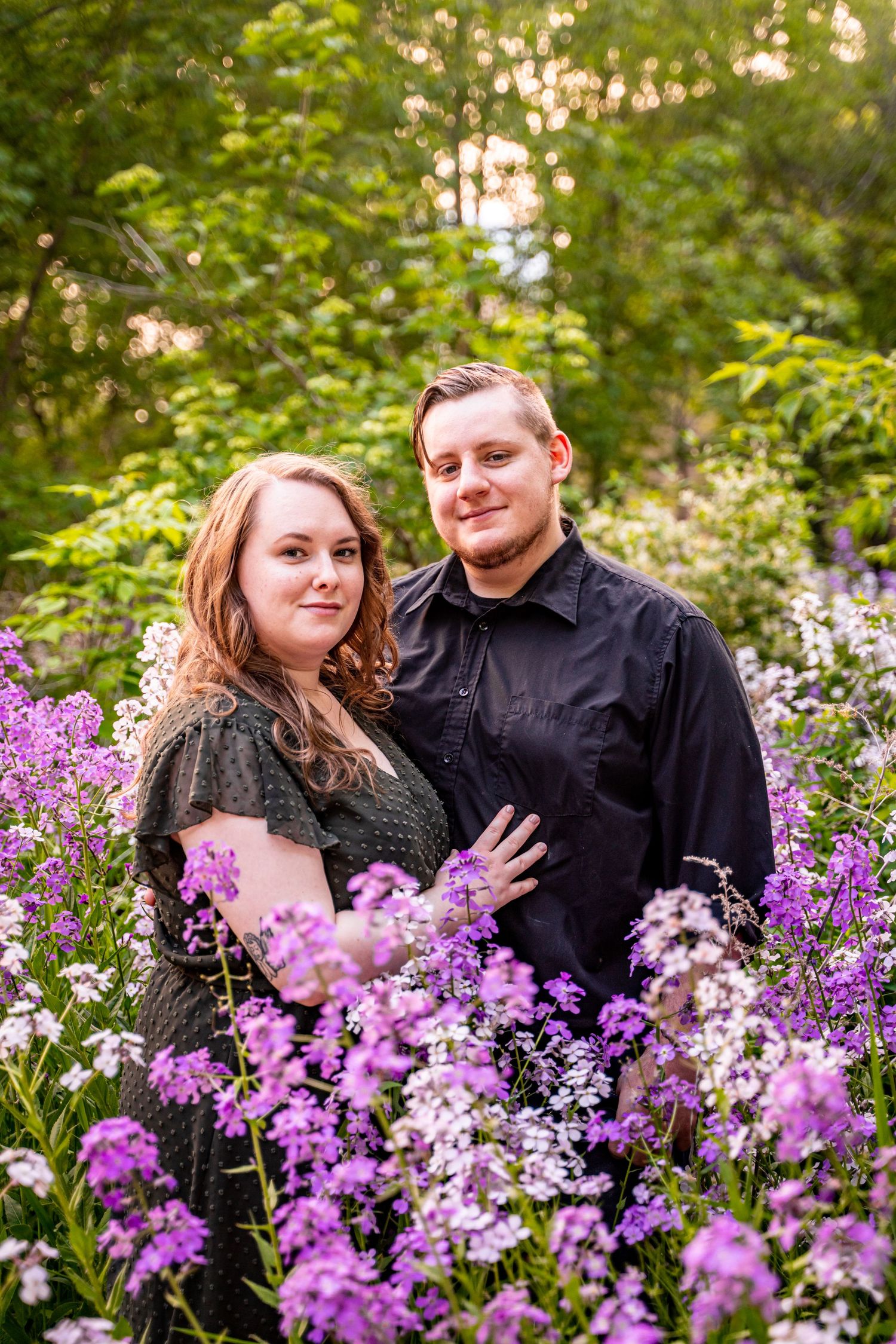 Couple posing romantically among purple and white wildflowers with lush green trees in background. engagement photography in wisconsin
