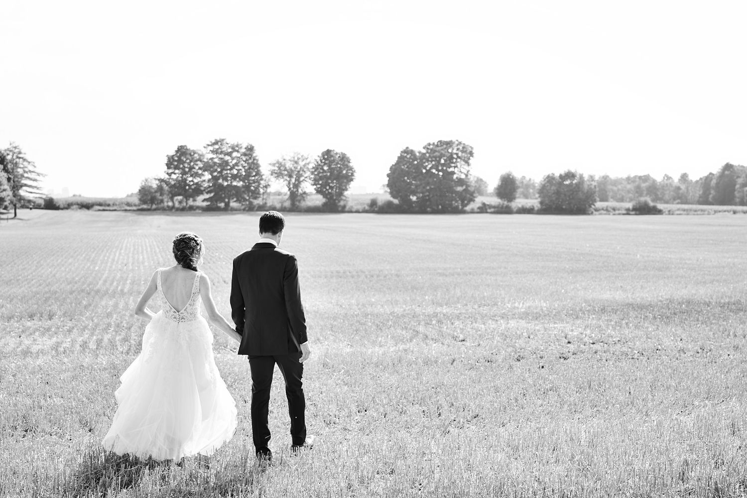 Black and white wedding photo showing newlyweds standing together in an open field looking at the horizon.
