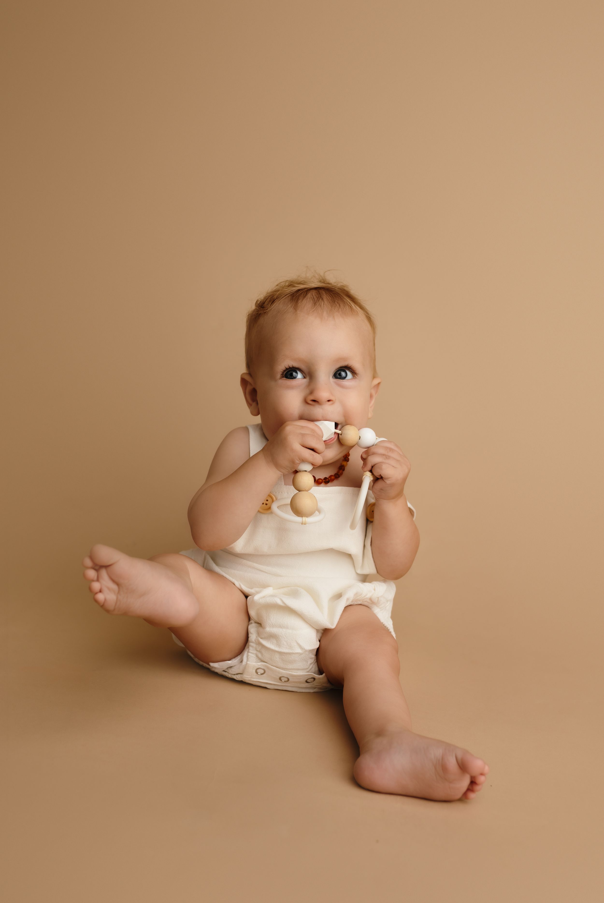 Harrisonburg photographer, baby, newborn, family, maternity, baby boy sitter against tan backdrop smiling with beads