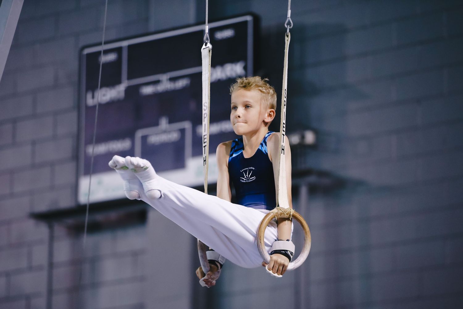 Young gymnast performs routine on rings in indoor gymnasium.